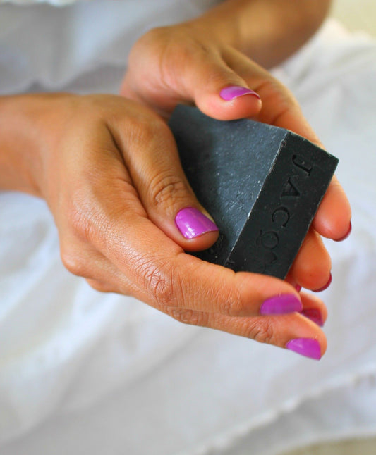 Black woman holding JACQ's activated charcoal face cleansing bar
