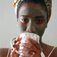 Black woman wearing JACQ's green smoothie face mask, drinking tea