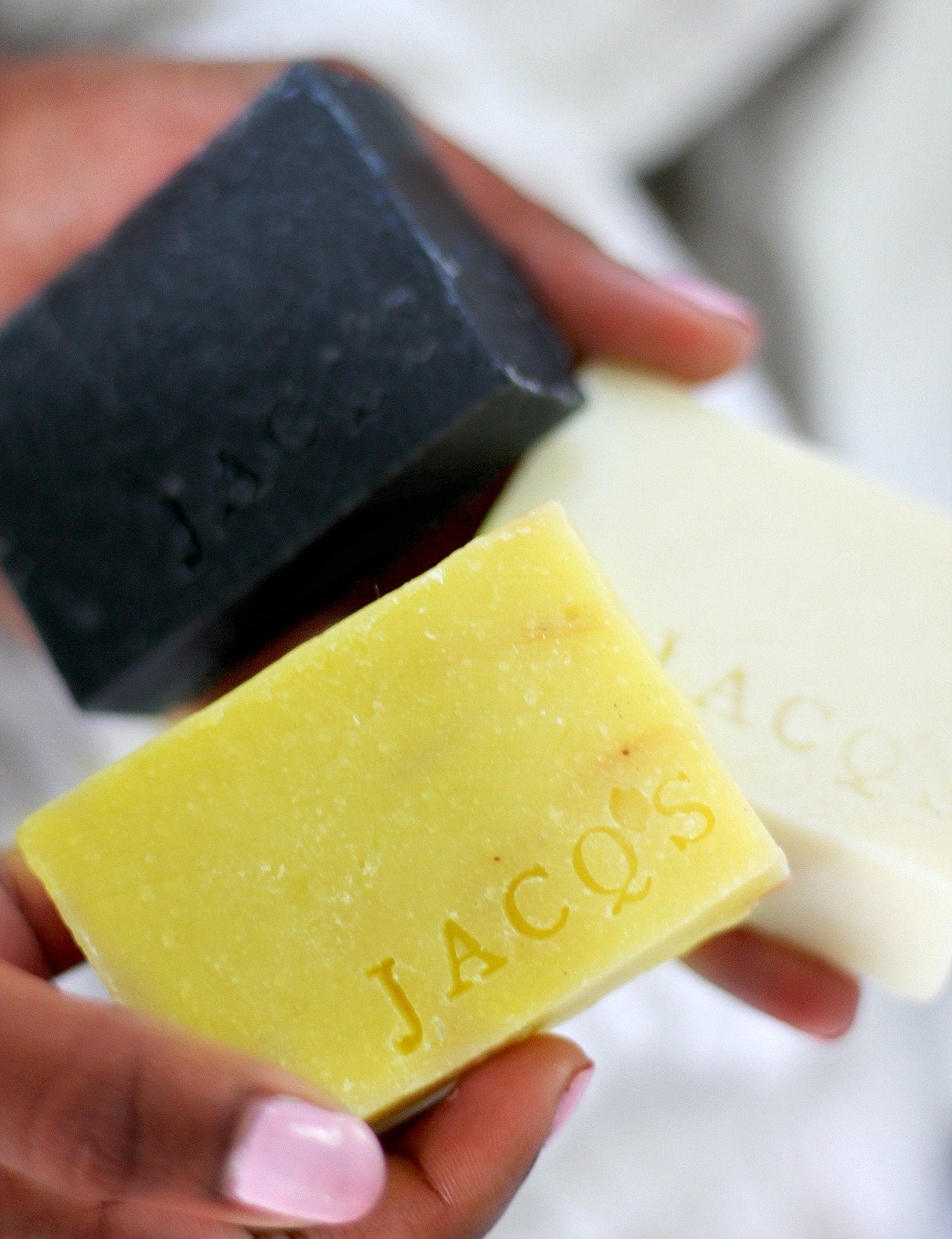 Black woman holding 2 JACQ's beauty bars, charcoal, and beige