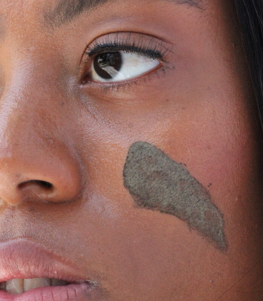 Black woman using JACQ's detoxifying charcoal face mask 